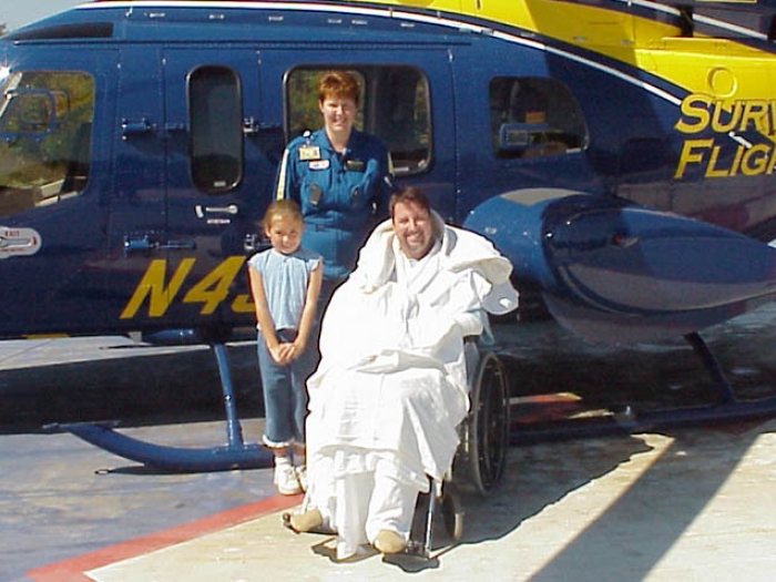 survival flight patient and daughter with employee in front of yellow and blue Michigan helicopter