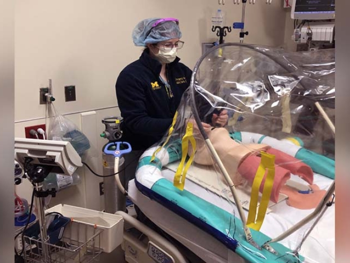 man with mask in hospital room reaching into portable negative pressure procedural tent