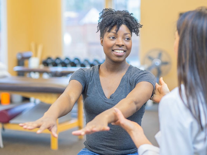 woman stretching out arms and a female physical therapist holding her one arm and talking with her