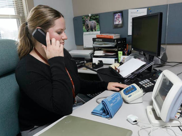 woman sitting at desk wearing black shirt and on phone while reading blood pressure