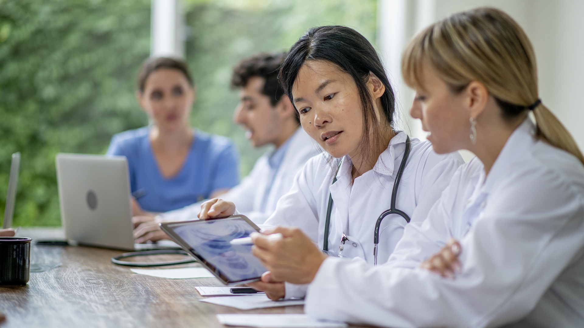 Group of diverse medical students at a table with female Asian student and blonde student in foreground