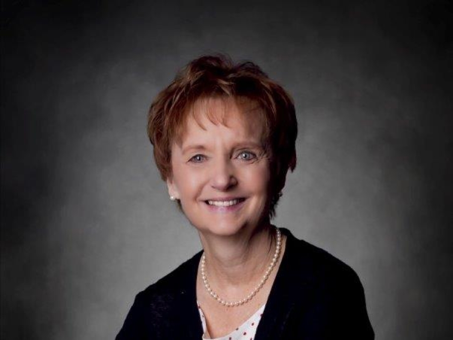 Smiling woman with reddish brown hair and hands folded wearing white blouse with black dots under black cardigan