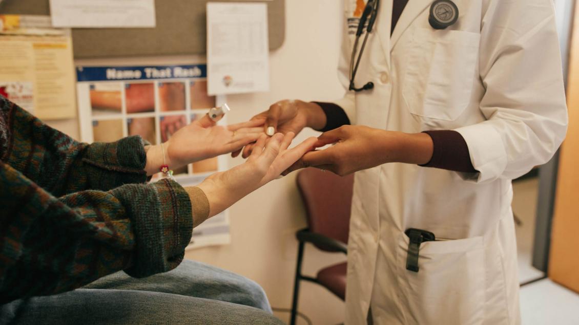 Hands and arms of white seated female patient and standing Black doctor
