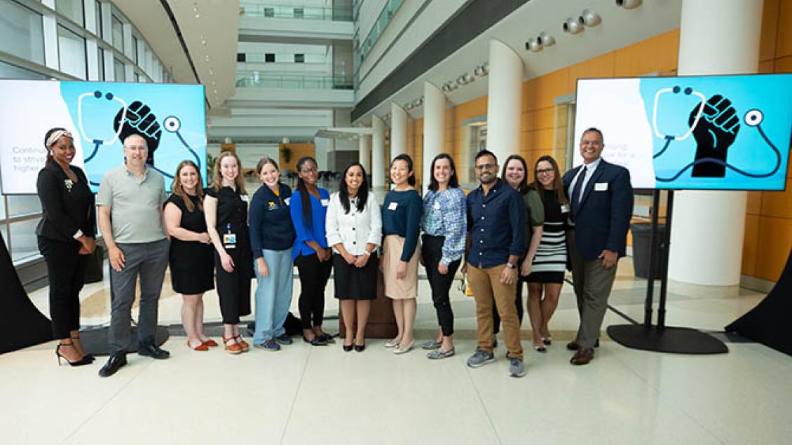 Group of diverse studentts and faculty standing in medical buidling with Black power fist with stethoscope art in background