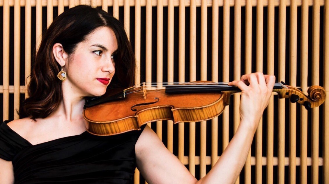 Dark-haired woman in black dress holding violen with slatted wooden background