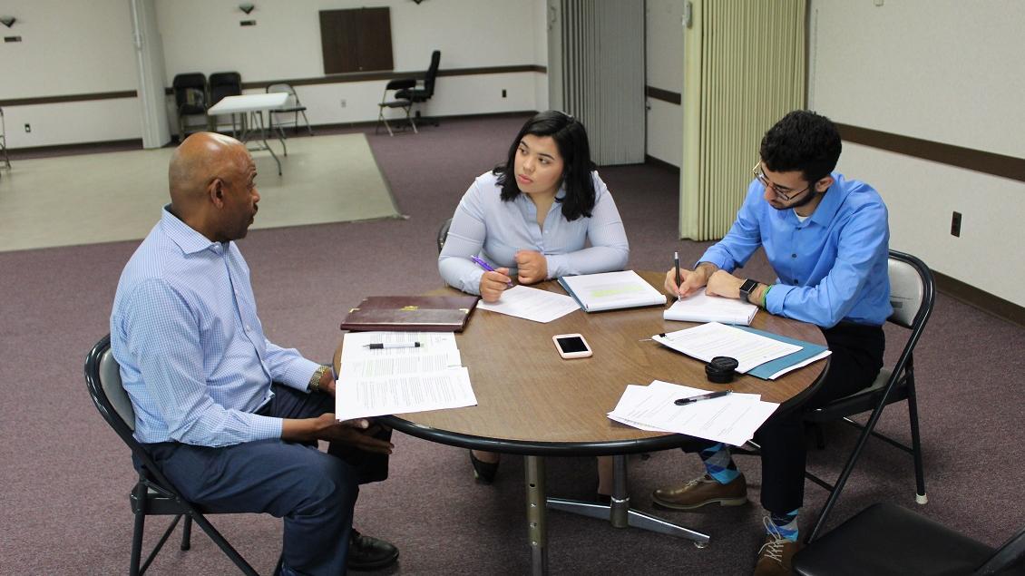 Group of people discussing and taking notes while sitting at a round table.