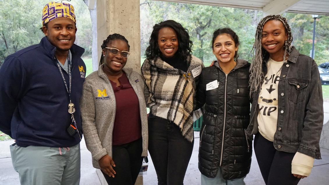 Group of black and brown people wearing coats and jackets and smiling with arms around each other