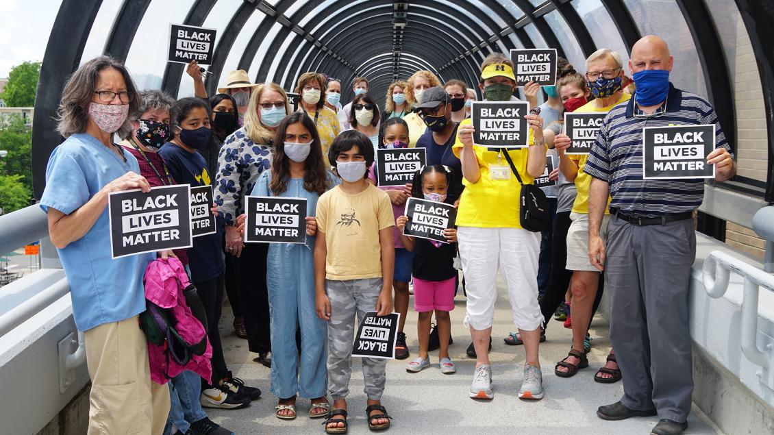 Diverse group of adults and children standing on bridge wearing masks and holding Black Lives Matter signs