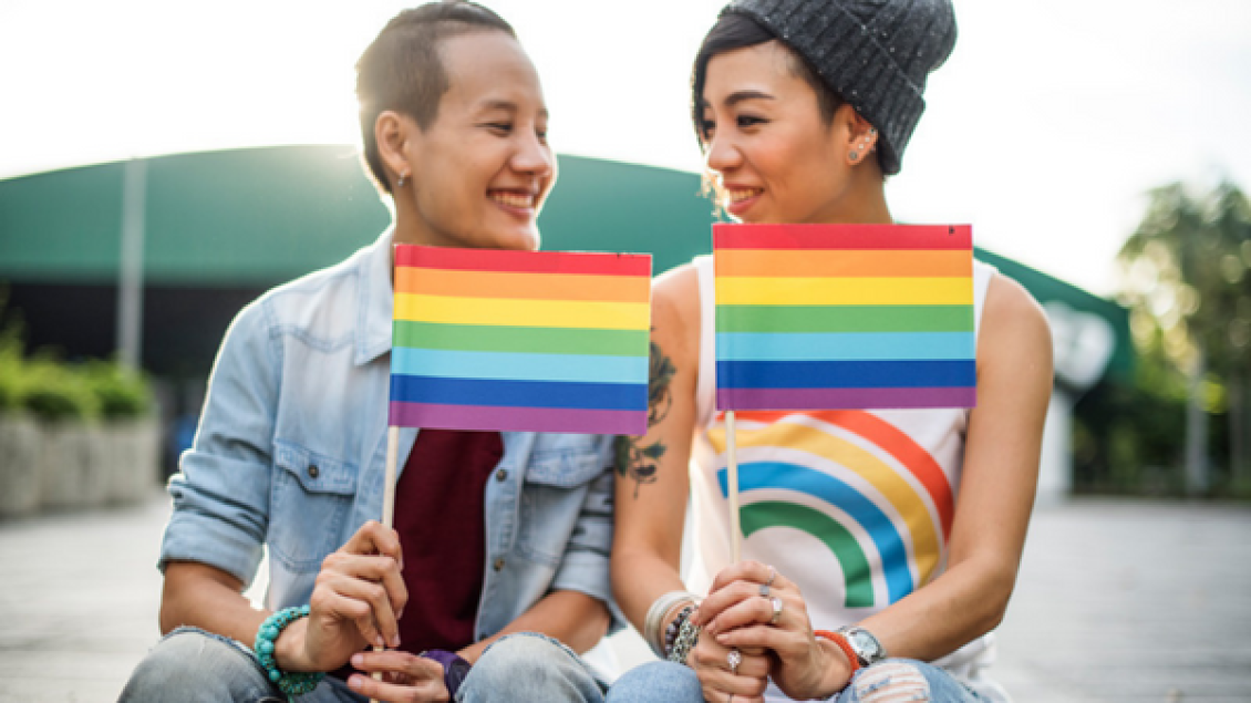 Stock photo of two young people are sitting outside holding Pride flags