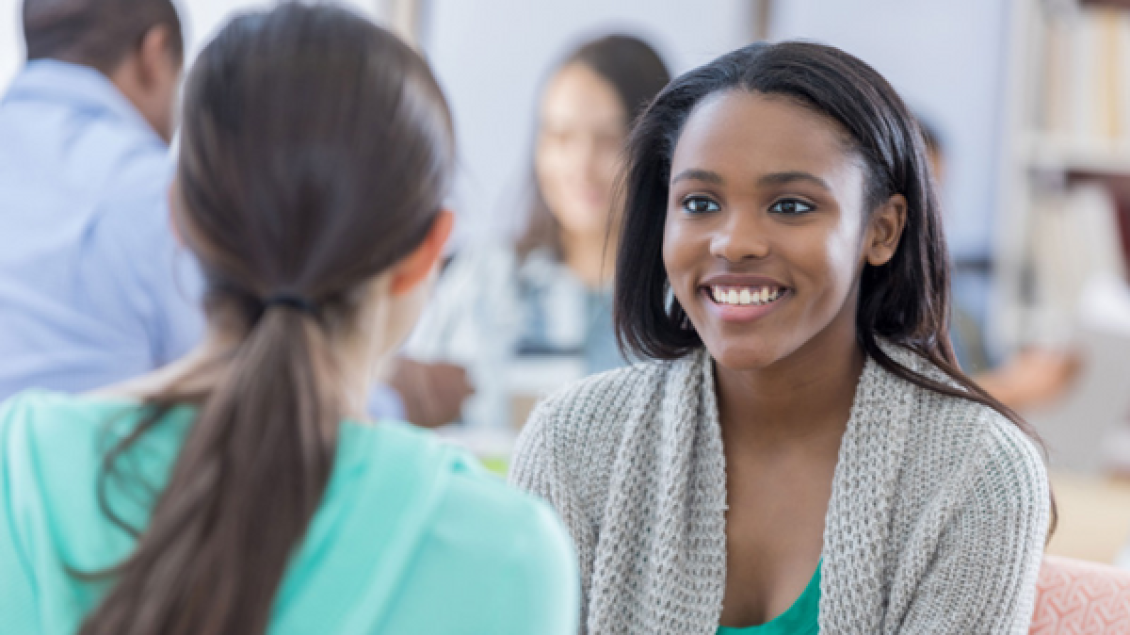 Two girls smiling and talking to each other.