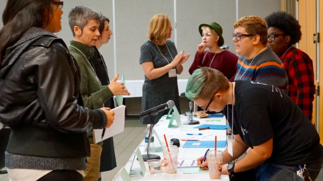 Group of people writing and discussing around information desk.