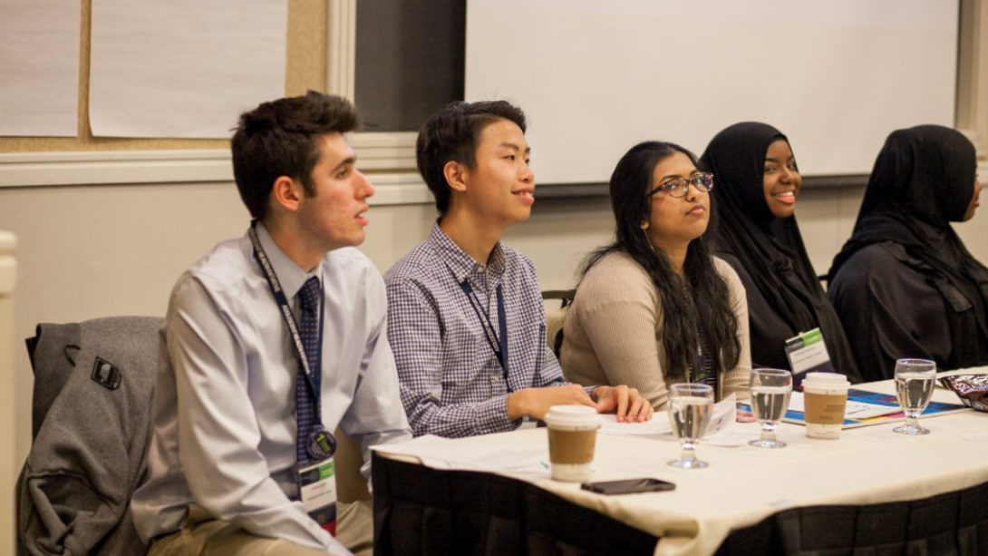 Group of teens sitting at one side of a table, listening