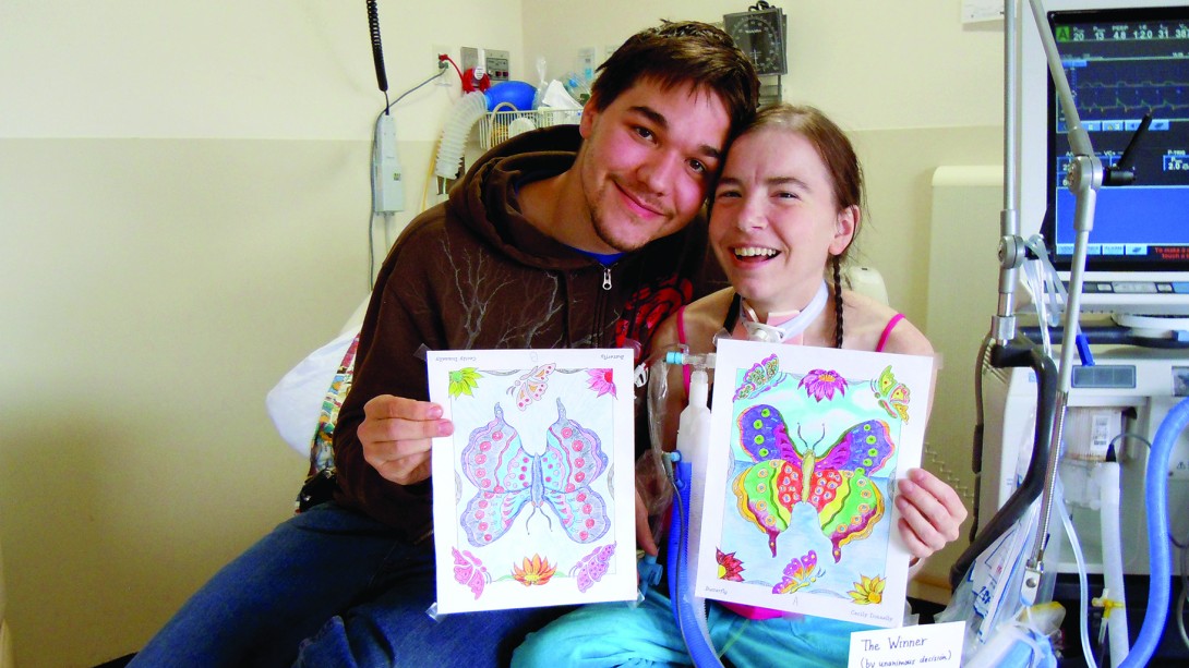 Young man and girl smiling and holding up art in hospital room