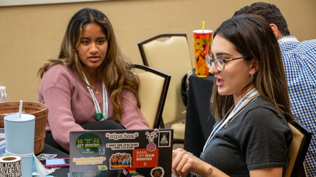 Two female youth talking and looking at a laptop covered with stickers