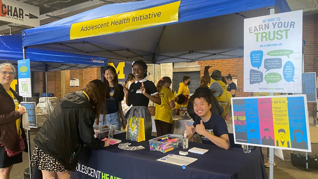 Group of youth working at a table in Adolescent Health Initiative tent