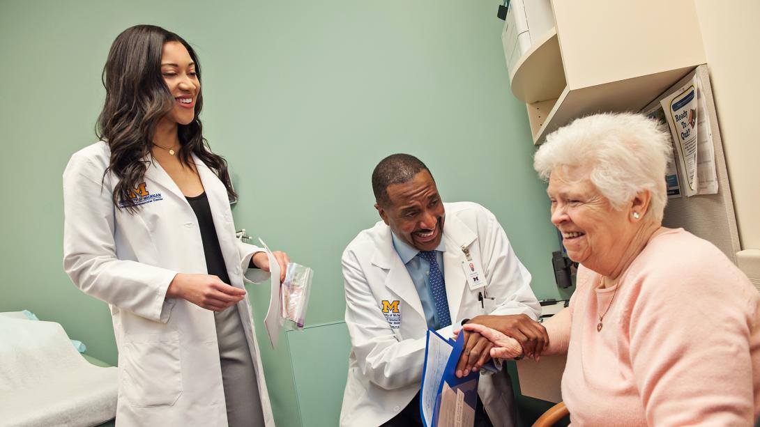Female and male black doctors laughing with seated elderly white female patient