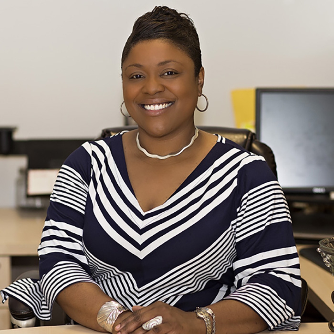 Smiling black woman wearing black and white striped dress seated with hands clasped in front