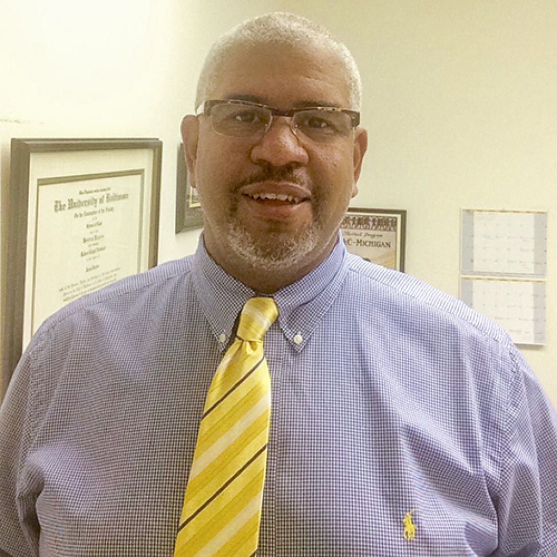 Smiling black man with glasses wearing blue shirt and yellow striped tie